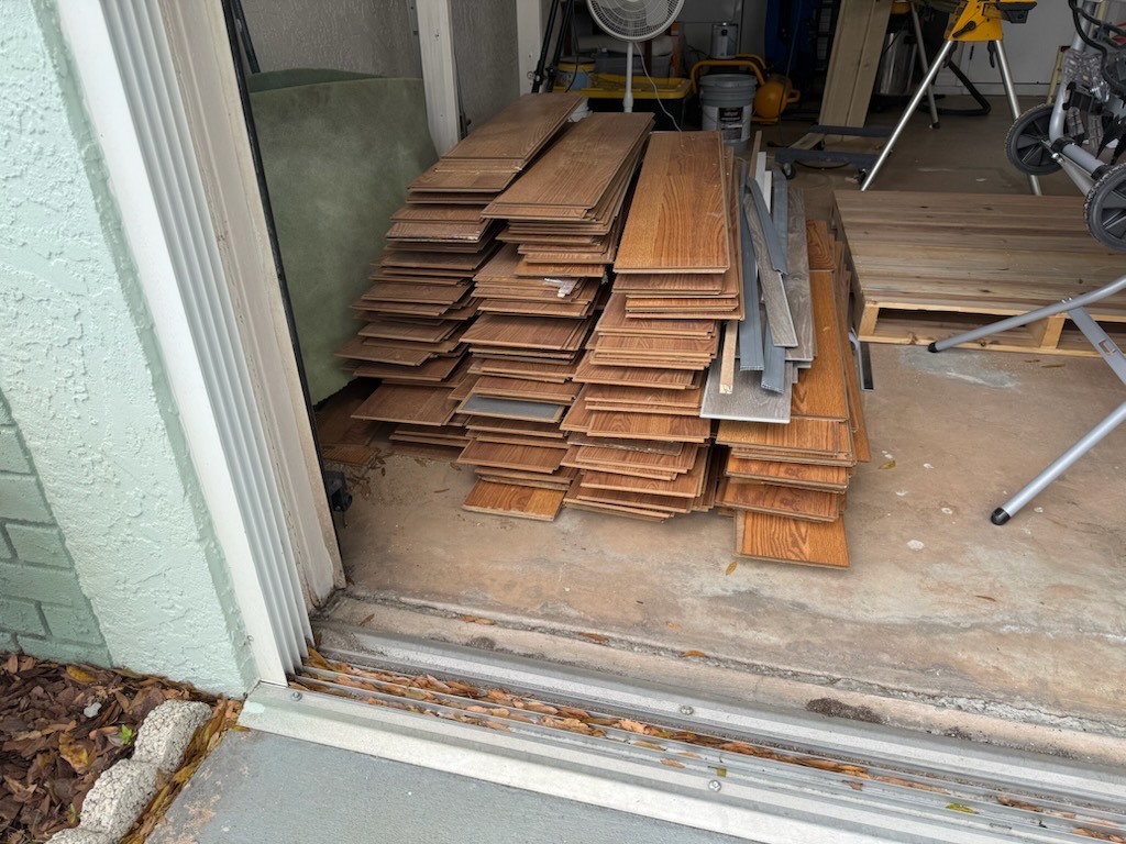 A pile of wooden planks stacked inside a garage, with tools and equipment in the background.