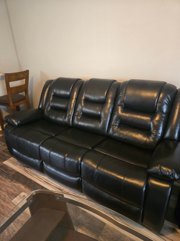 A black leather sofa with a modern design, featuring padded seats and armrests, positioned in a room.